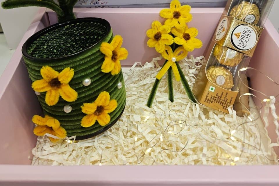A sunflower rakhi hamper — a green pot, a sunflower posy, chocolates and fairy lights in a pink keepsake box